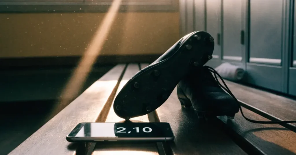 Eine Reihe Sportschuhe steht auf einer Bank in einer Umkleide, Licht fällt aus einem hohen Fenster.