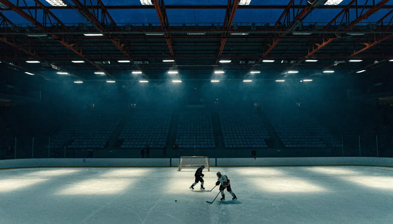 Ein grosses Eisstadion aus der Ferne gesehen, hell erleuchtet von Flutlicht in der Abenddämmerung, davor eine leere Strasse.