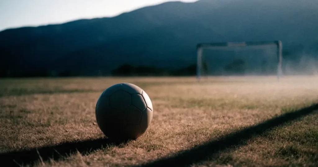 Ein Fussball auf einem staubigen Rasenstück in der Abendsonne, im Hintergrund eine hohe Bergkette