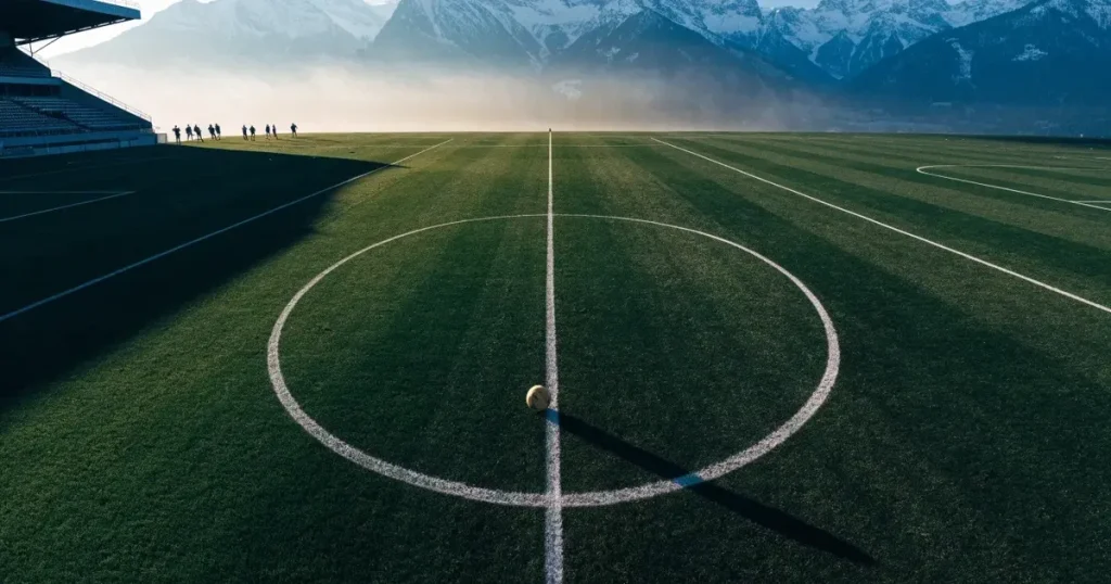 Ein Fussballplatz aus der Vogelperspektive mit sauberen Linien auf dichtem Rasen, in der Ferne verschneite Berge.