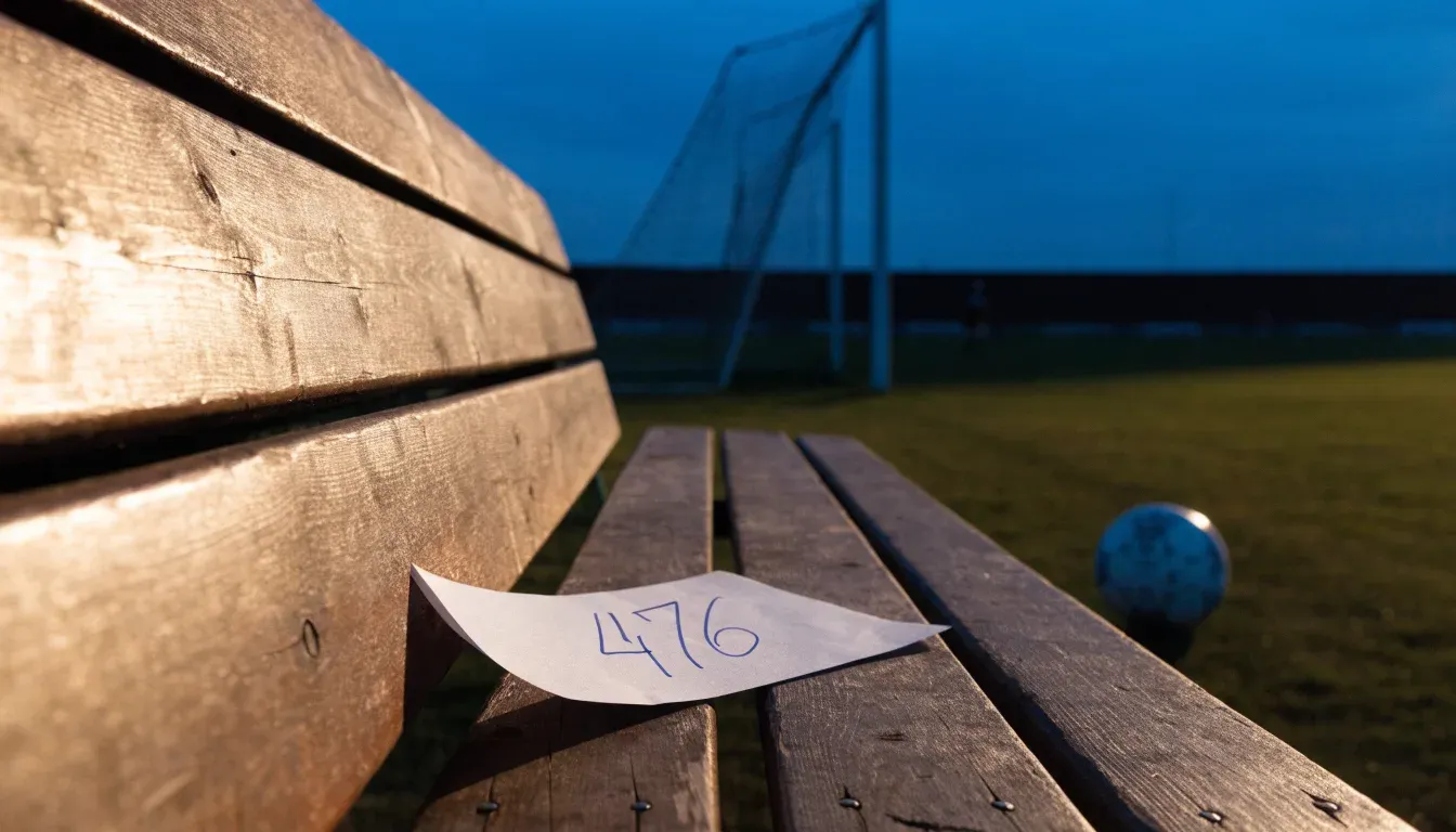 Ein Fussballschuh hängt an den Schnürsenkeln an einem Zaunpfosten neben einem Trainingsplatz im Abendlicht.