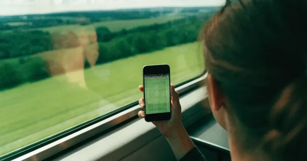 Eine Hand hält ein Smartphone mit schwarzem Bildschirm vor einem Zugfenster, draussen ziehen Hügel und Wiesen vorbei.