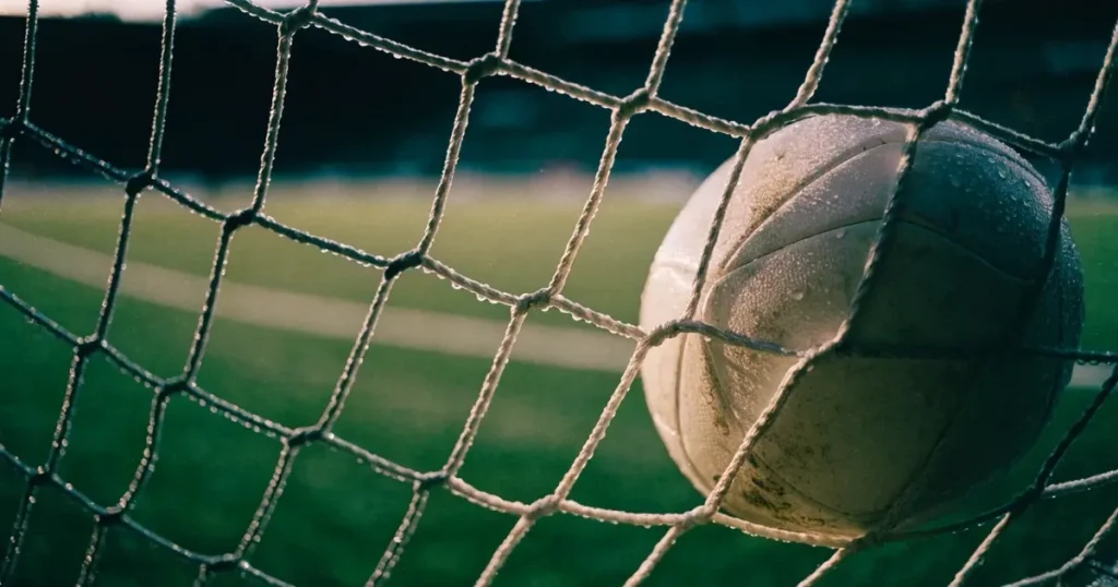 Ein Fussballnetz in Nahaufnahme, in dem ein Ball hängt, Wassertropfen glänzen auf den Maschen.